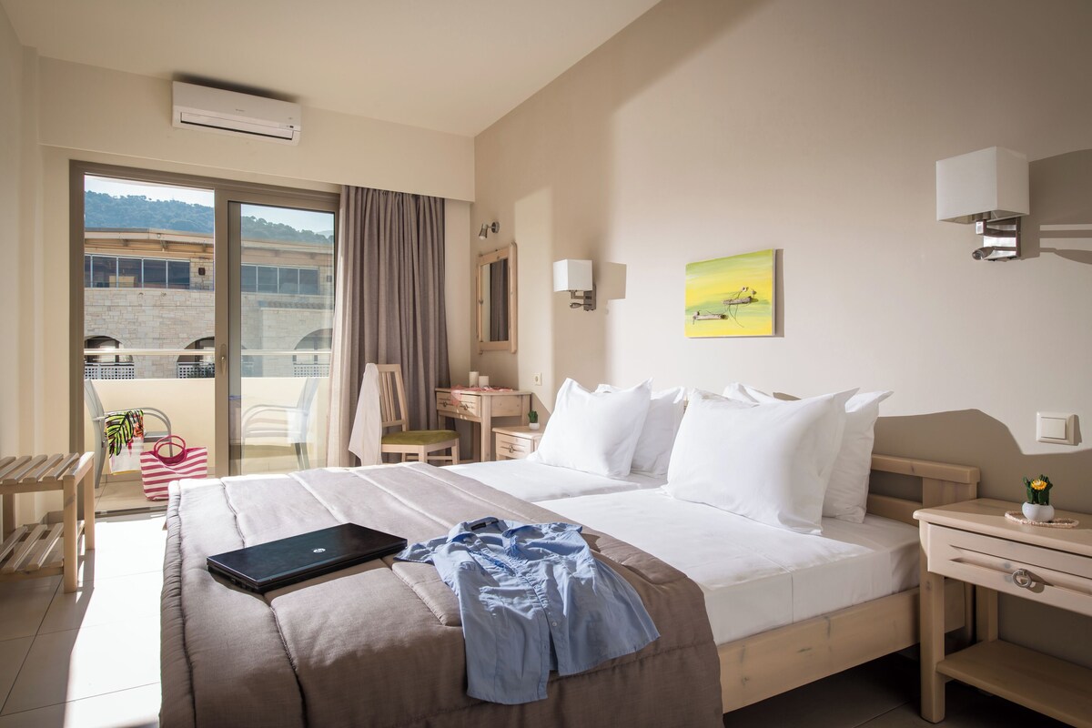 Ein Hotelzimmer mit Bett, Schreibtisch, Stuhl, einem Fenster mit Aussicht und einem Balkon.