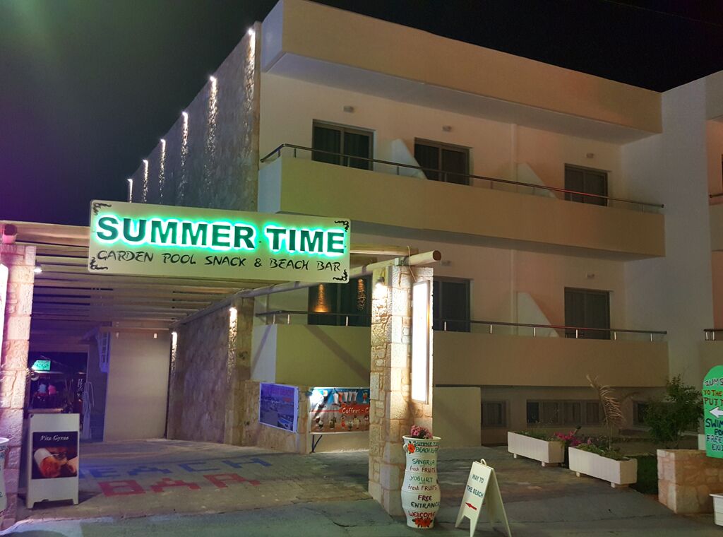 En bygning med flere etager med skilt, der viser "SUMMER TIME", og henviser til swimmingpool, snackbar og strandbar.