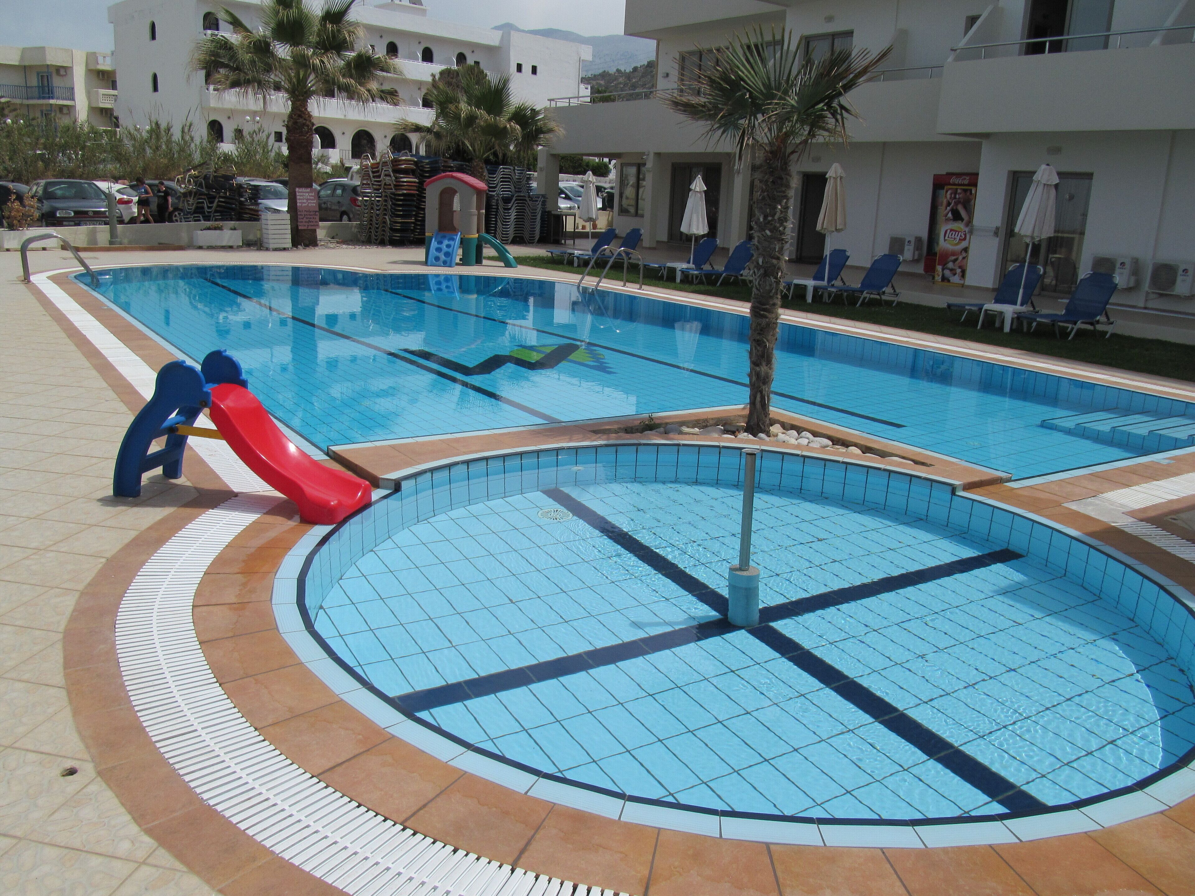 A swimming pool with a slide, lounge chairs, and palm trees.