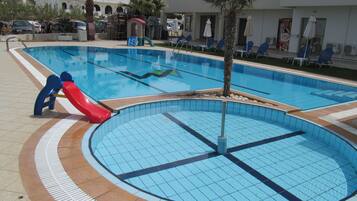 A swimming pool with a slide, lounge chairs, and palm trees.