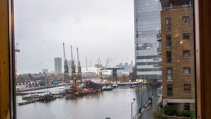Vista de un puerto con barcos y grúas, edificios al fondo y un día lluvioso.