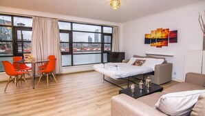 Una habitación de hotel moderna con un ventanal grande, una cama, un sofá, una mesa de comedor con sillas y un cuadro en la pared.