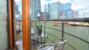 Un balcón con vistas a edificios altos, una mesa pequeña con una planta en maceta y una silla.