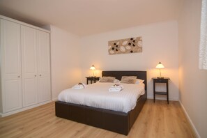 A bedroom with a large bed, two bedside tables, a nightstand, a wardrobe, and a wall-mounted artwork.