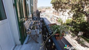 Un balcón con una silla, plantas en macetas y vistas a la calle y edificios.