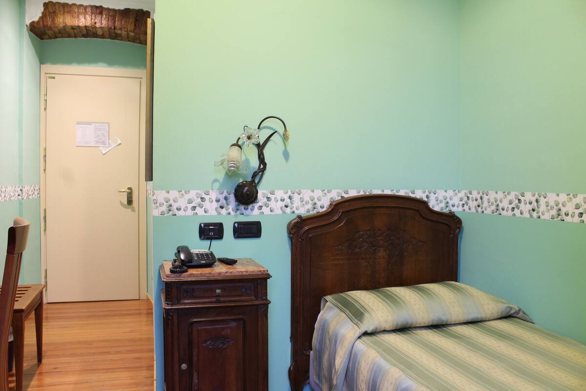 Une chambre à coucher avec un lit, une commode en bois, un téléphone et une lampe fixée au mur.
