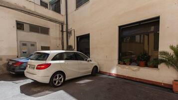 A white car parked in a narrow alleyway with a building on one side and a window with potted plants on the other.