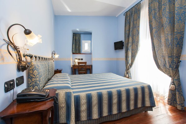 Una habitación de hotel con una cama, un escritorio con teléfono, un espejo y cortinas.