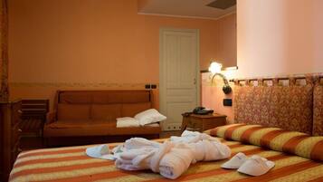A hotel room with a bed, a sofa, a nightstand, and a door.