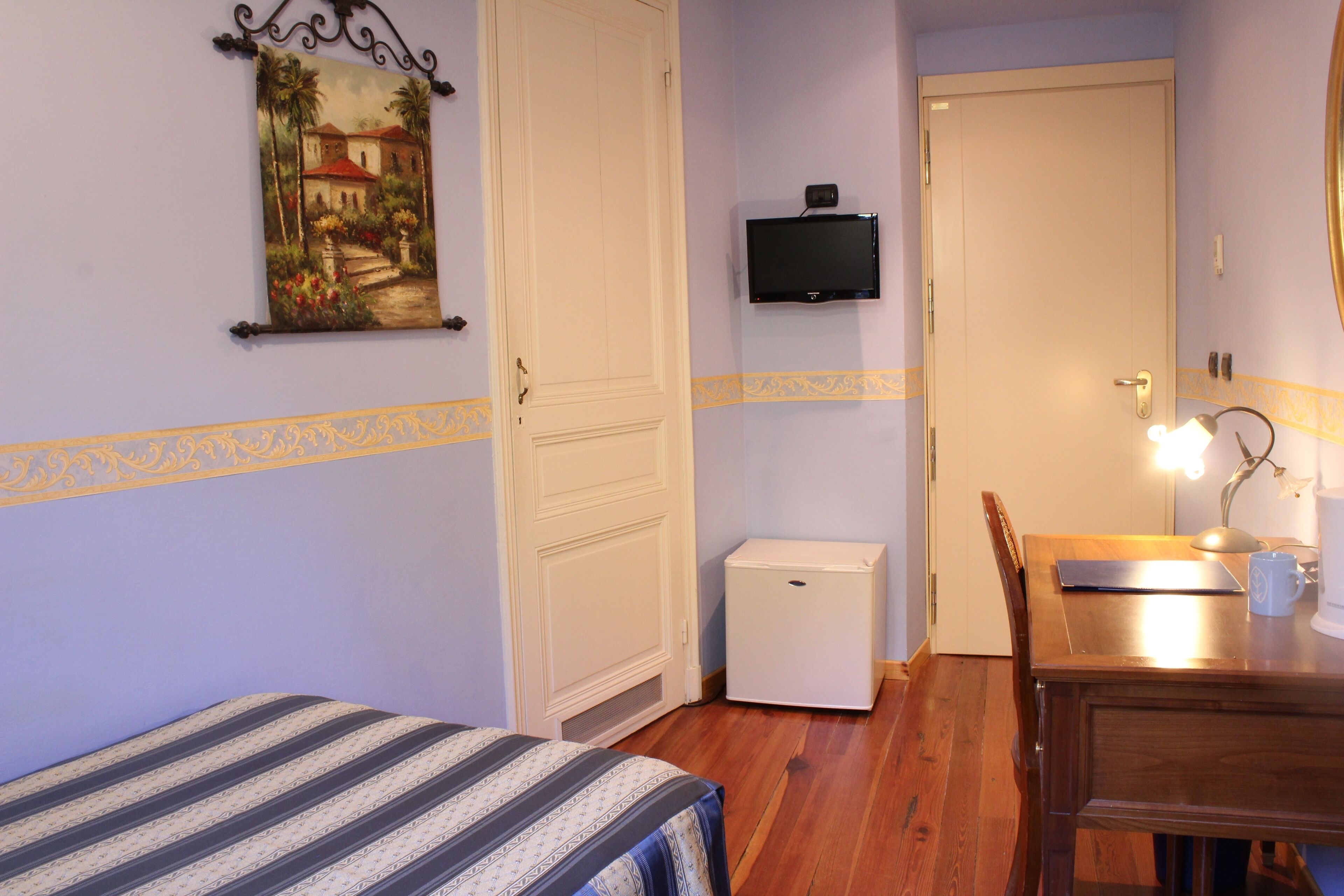 A room with a bed, a desk with a lamp, a television, and a refrigerator.
