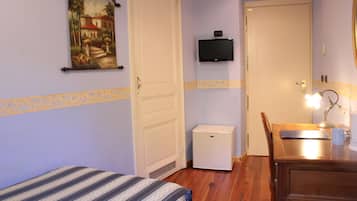 Et værelse med seng, skrivebord med lampe, fjernsyn og køleskab.