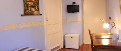 A room with a bed, a desk with a lamp, a television, and a refrigerator.