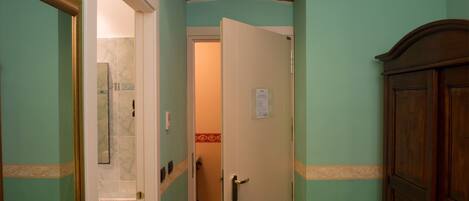 Un pasillo con un baño a la izquierda, una puerta con un aviso en la pared y un armario de madera a la derecha.