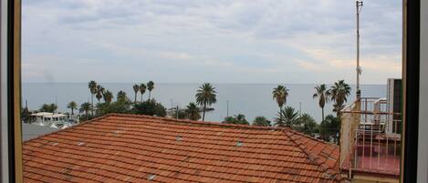 A view of a red-tiled roof from a balcony, with a clear sky and palm trees in the background.