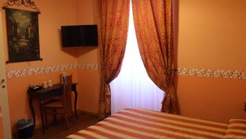 A hotel room with a bed, a desk with a chair, a television on the wall, and a painting.