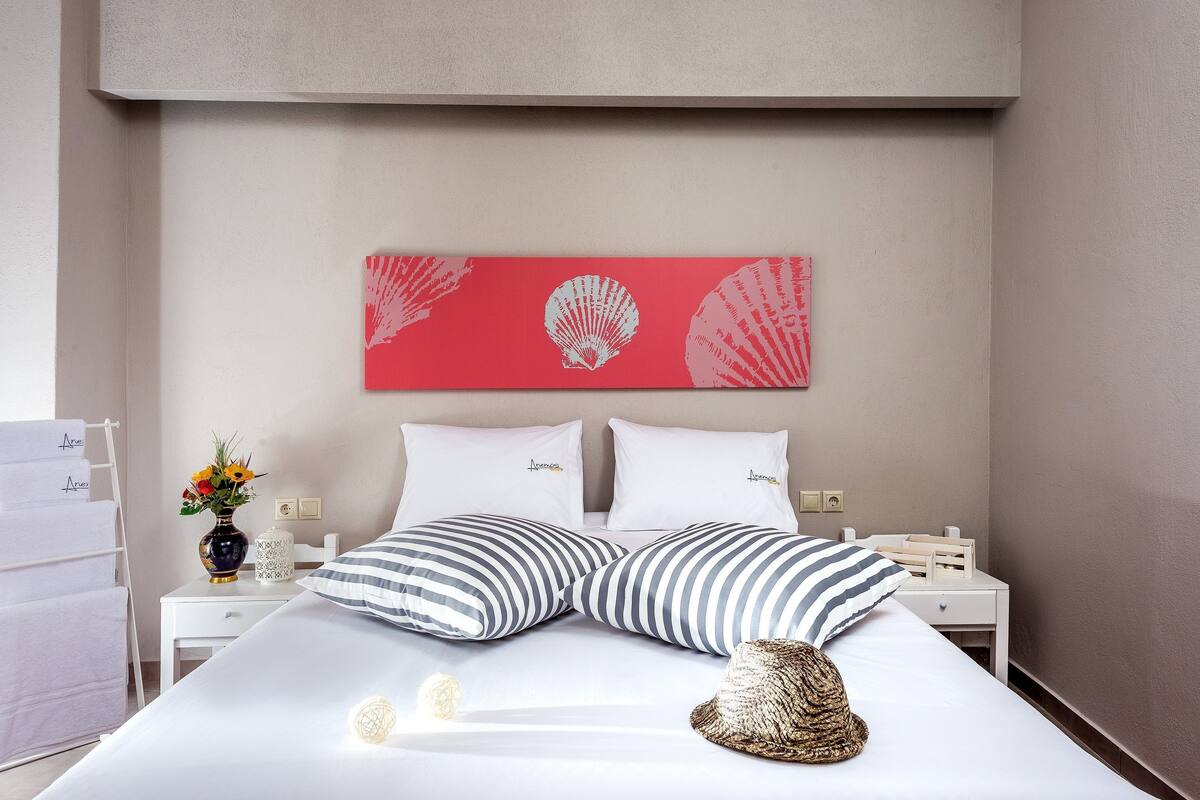 Una cama bien tendida con almohadas a rayas, un florero con flores y un adorno de pared.