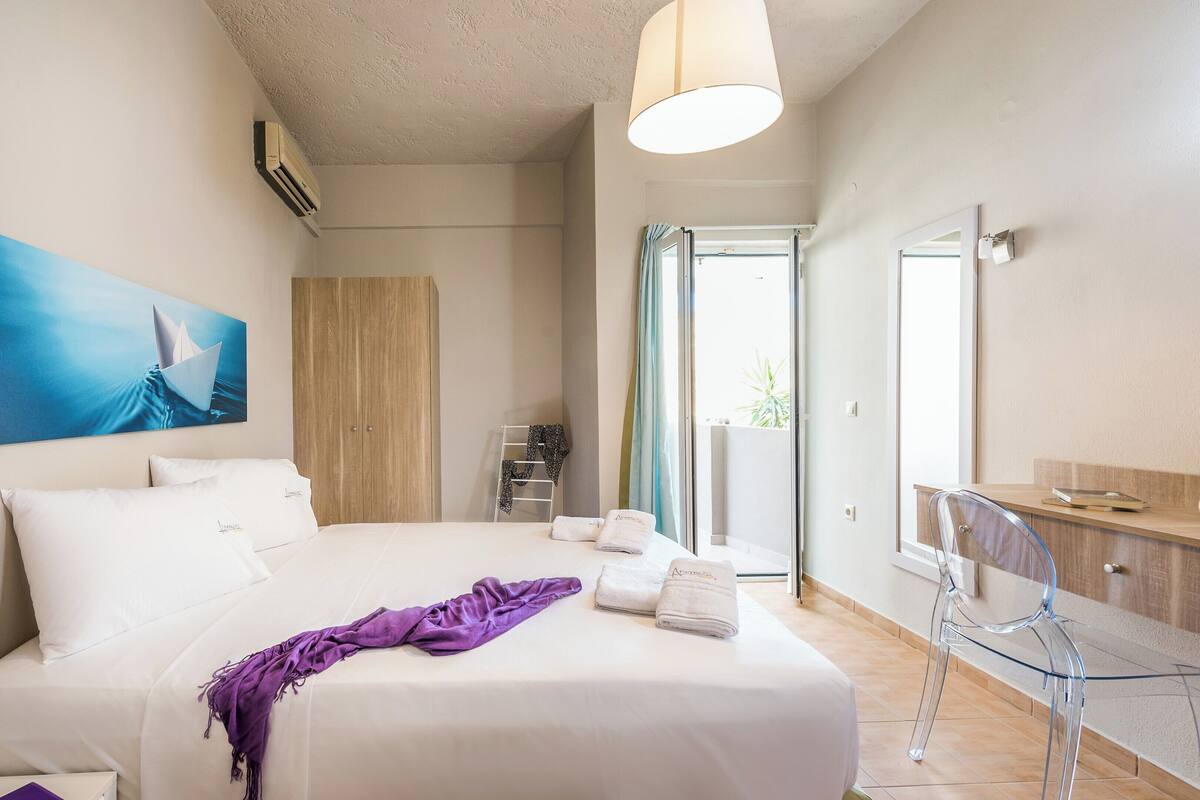Habitación de hotel con cama, baño, balcón y vistas al exterior.