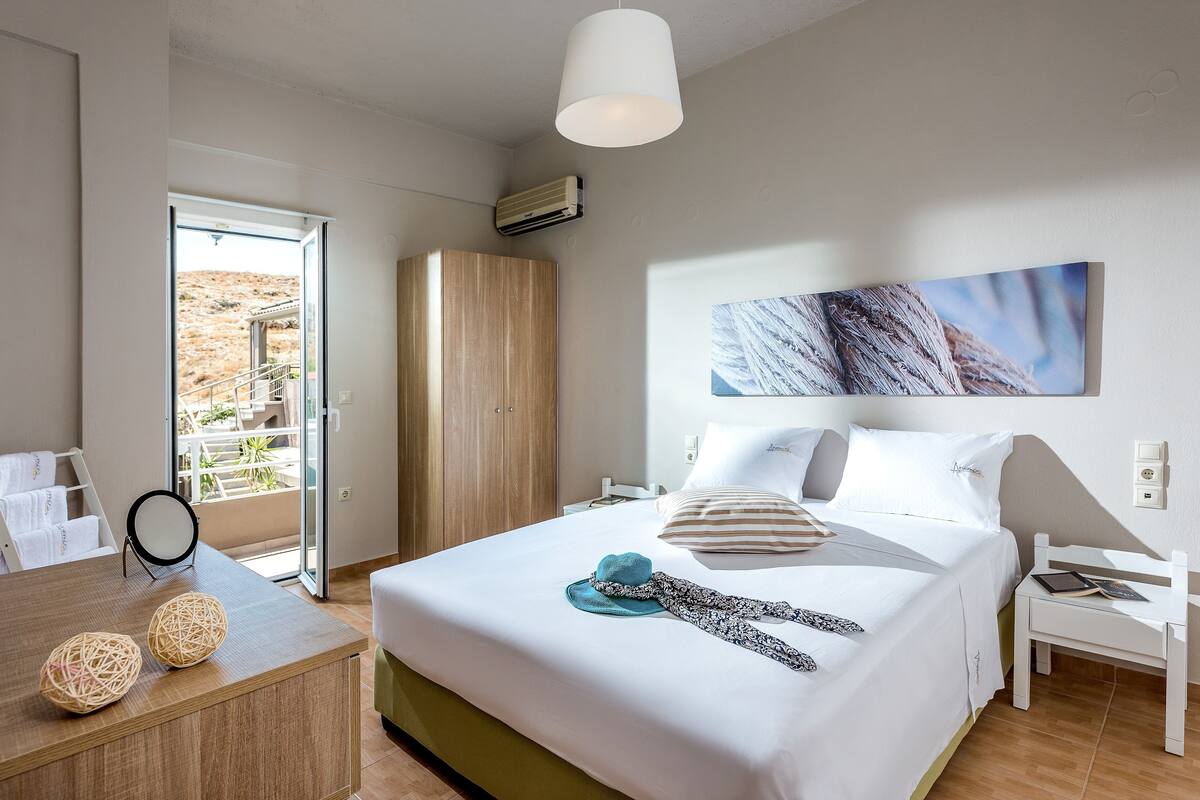 Habitación de hotel con cama, escritorio, silla, armario y un amplio ventanal con vistas.