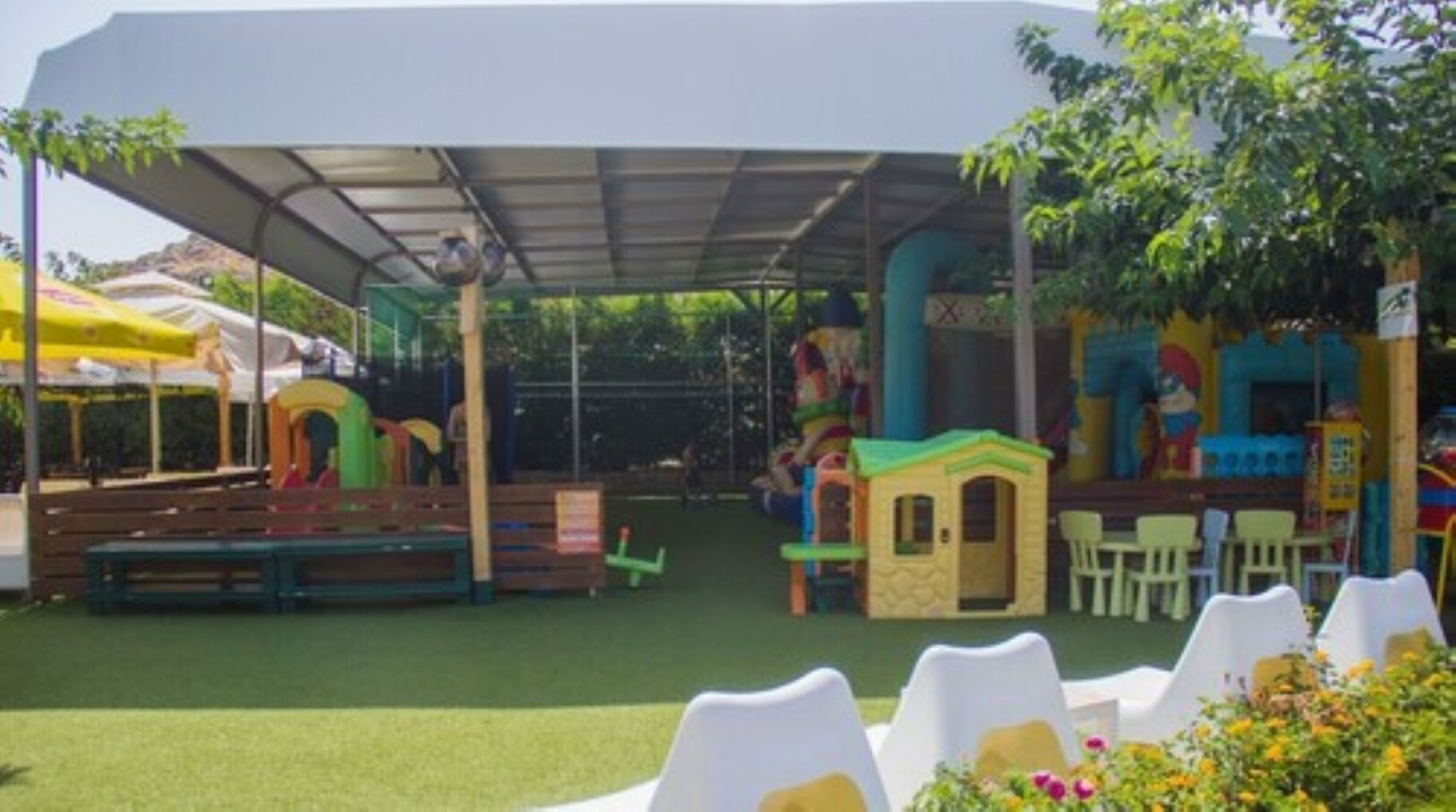 A covered outdoor play area with artificial turf, play structures, and seating.