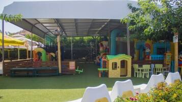 A covered outdoor play area with artificial turf, play structures, and seating.