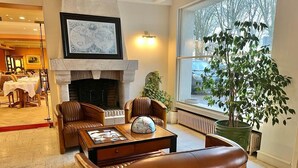 A cozy room with leather chairs, a fireplace, a large window with a view, and a dining area in the background. - Hôtel du Rivage (Gien)