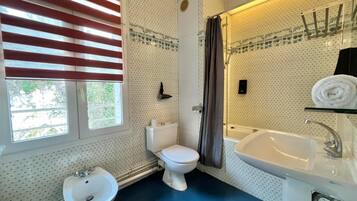 A bathroom with a bidet, toilet, sink, and a window with blinds.