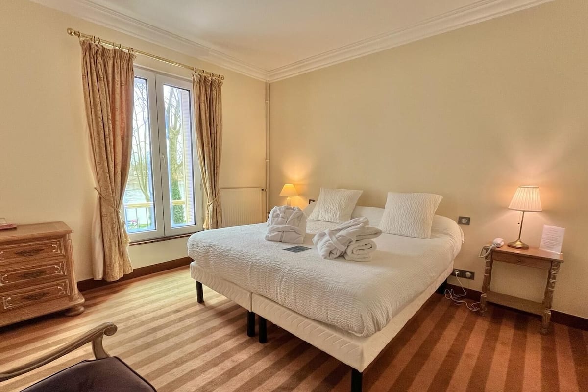 A hotel room with a large bed, two bedside lamps, a wooden nightstand, a desk, and a chair.