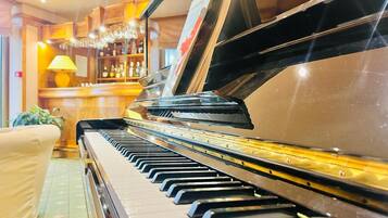 A grand piano in a well-lit room with a bar area in the background.