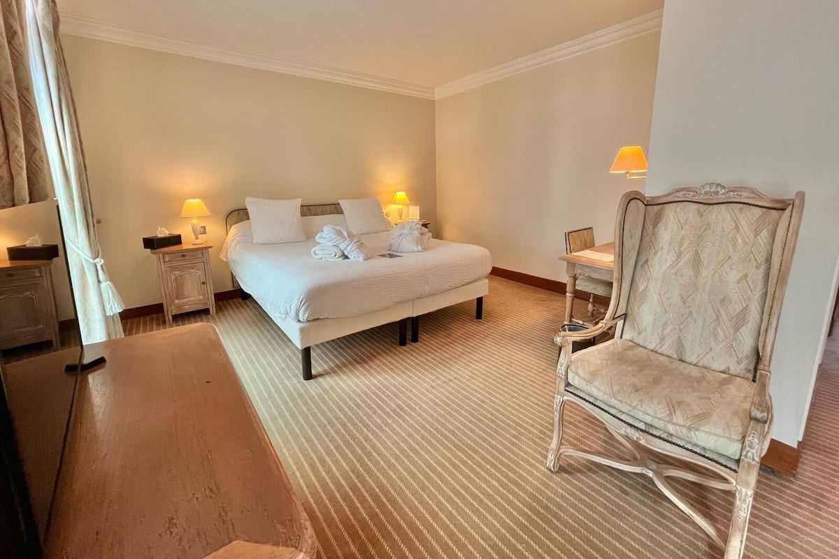 A hotel room with a bed, two bedside tables with lamps, a wooden chair, and a small table with a lamp.