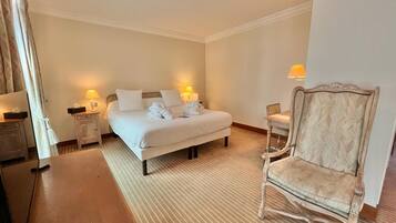 Una habitación de hotel con una cama, dos mesitas de noche con lámparas, una silla de madera y una pequeña mesa con lámpara.