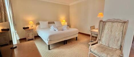 A hotel room with a bed, two bedside tables with lamps, a wooden chair, and a small table with a lamp.