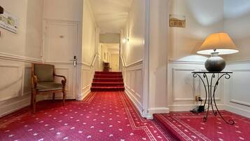 Un pasillo de hotel con alfombra roja, una silla, una lámpara y una escalera.