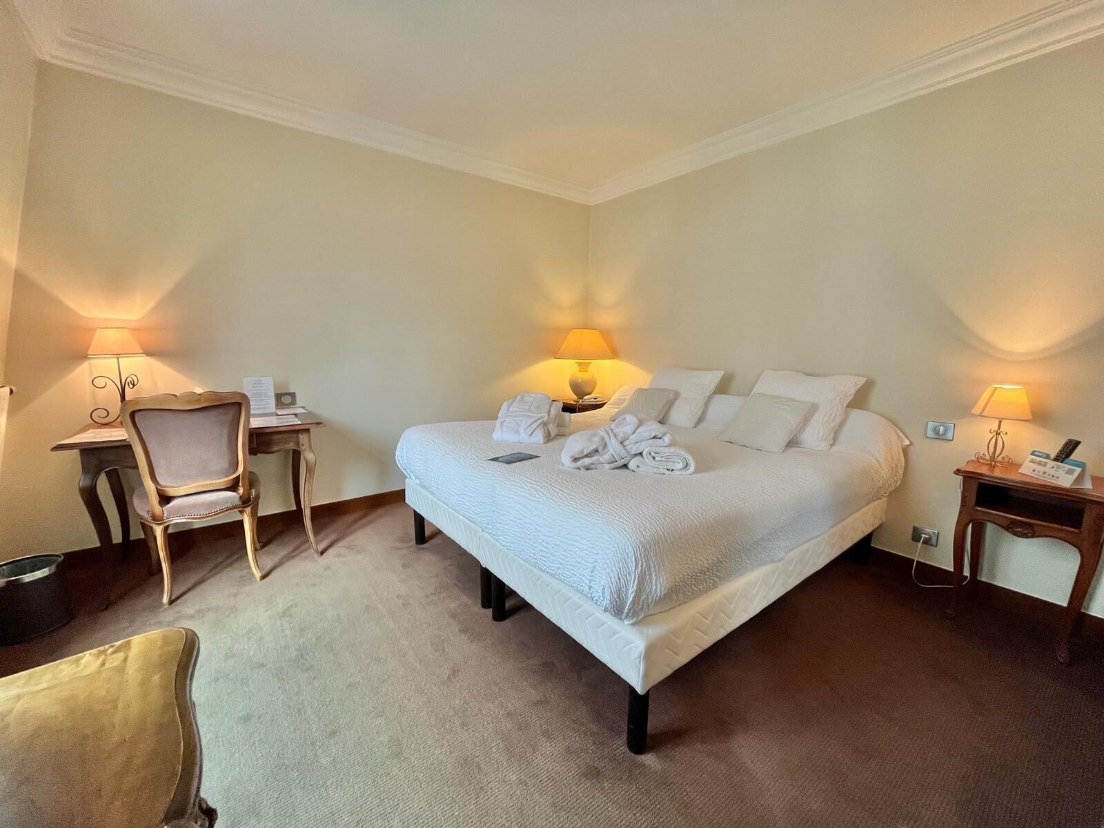 A neatly arranged hotel room with a large bed, two bedside tables, a desk, and a chair.