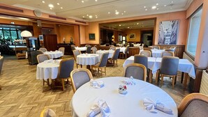 A dining area with round tables, chairs, and a kitchen in the background. - Hôtel du Rivage (Gien)
