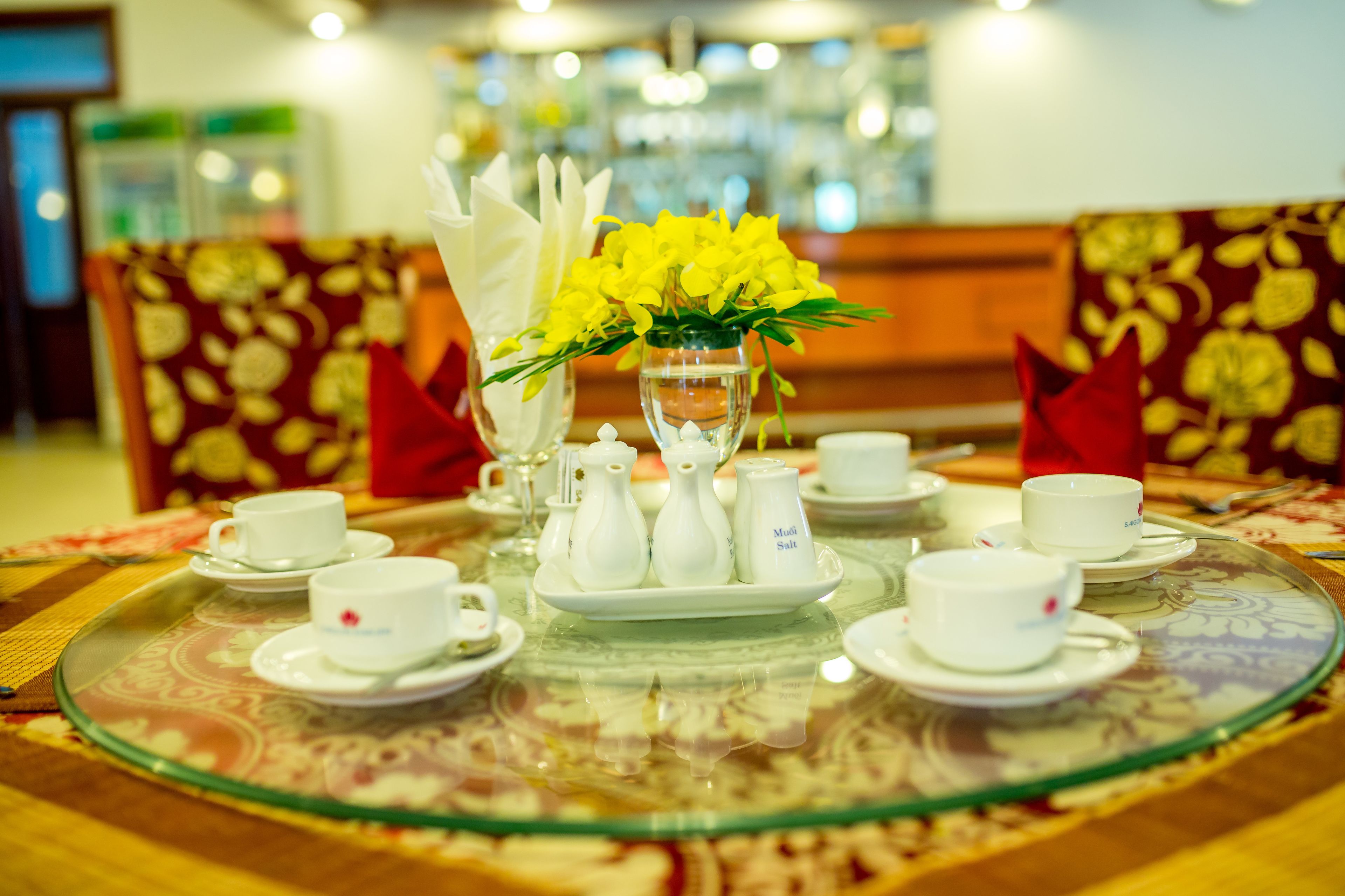 A dining table with white cups, saucers, and a glass tray set with a floral tablecloth.