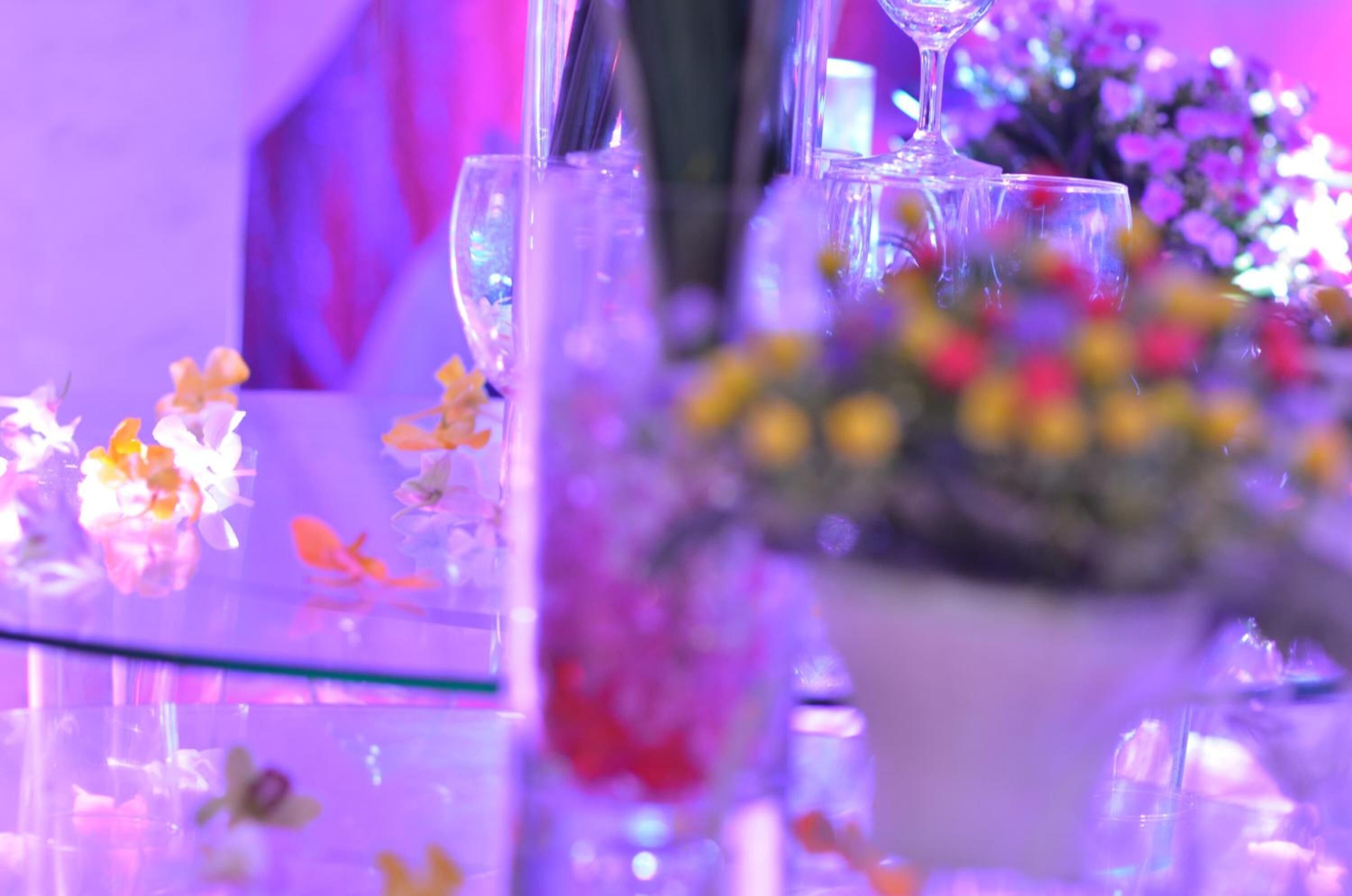 Un tavolo con piano in vetro, circondato da bicchieri e un vaso con fiori.