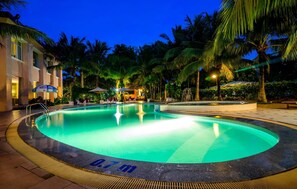 Une piscine entourée d’une terrasse, de palmiers et d’un bâtiment doté d’un espace extérieur aménagé pour s’asseoir.