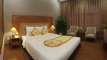 A hotel room with a large bed, two bedside tables with lamps, a small table with a vase, two chairs, and a curtain.
