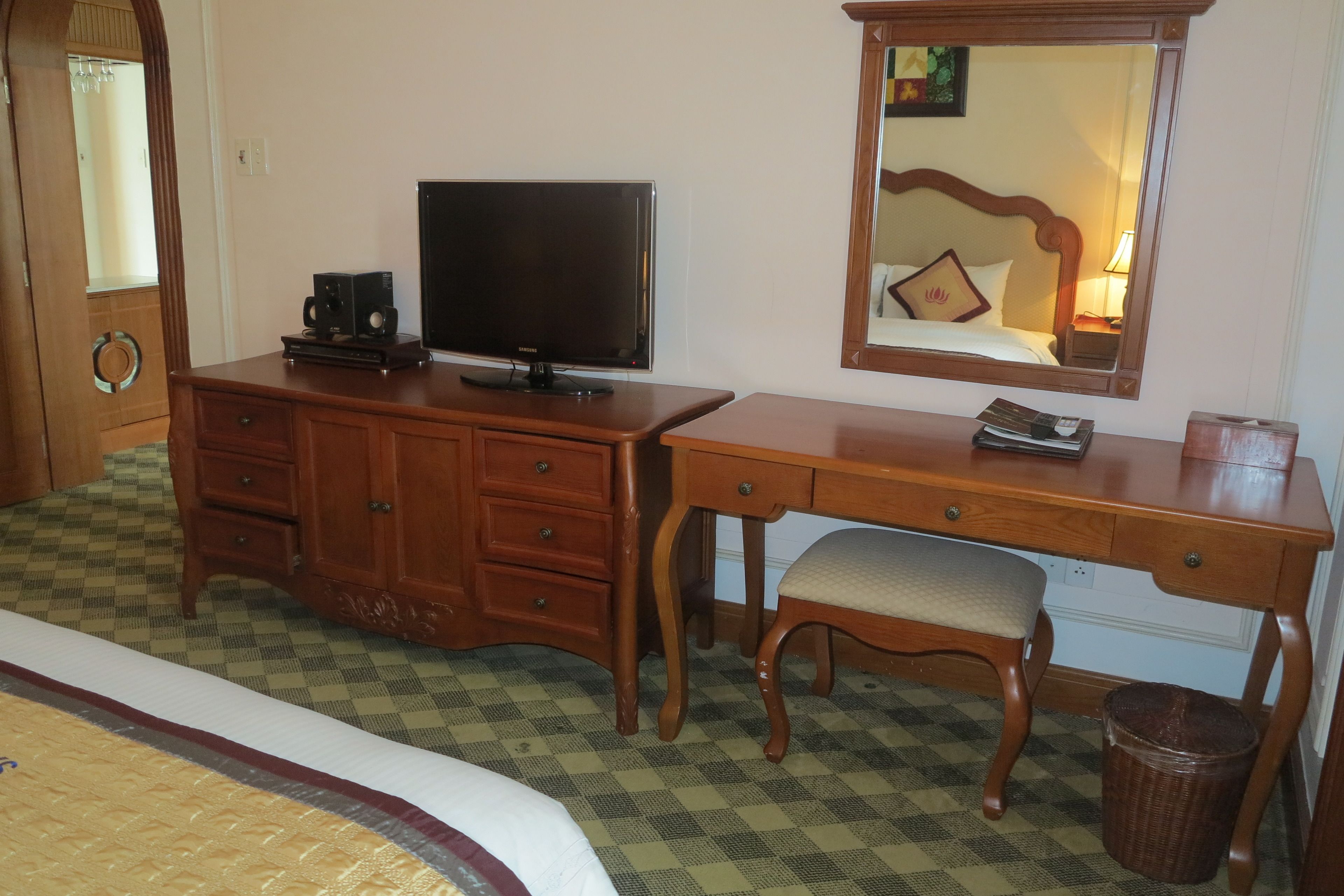 A hotel room with a wooden desk, a television, a chair, and a bed.