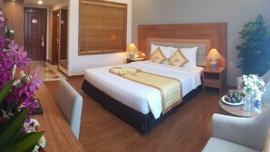 Una habitación de hotel con una cama grande, lámparas de noche, un cabecero de madera y una planta en maceta.