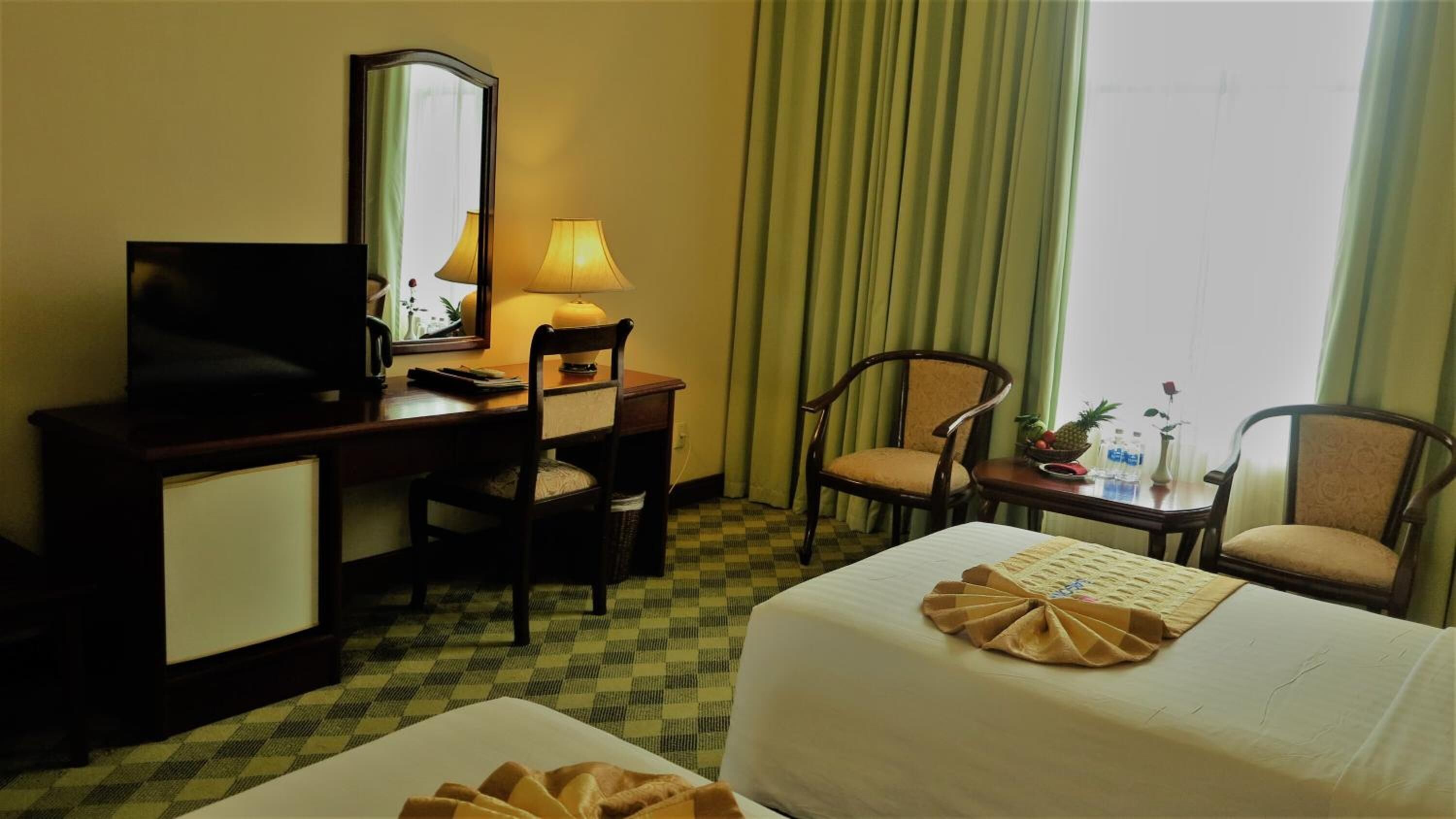 Habitación de hotel con escritorio, dos sillas, una cama, televisor y ventana con cortinas.
