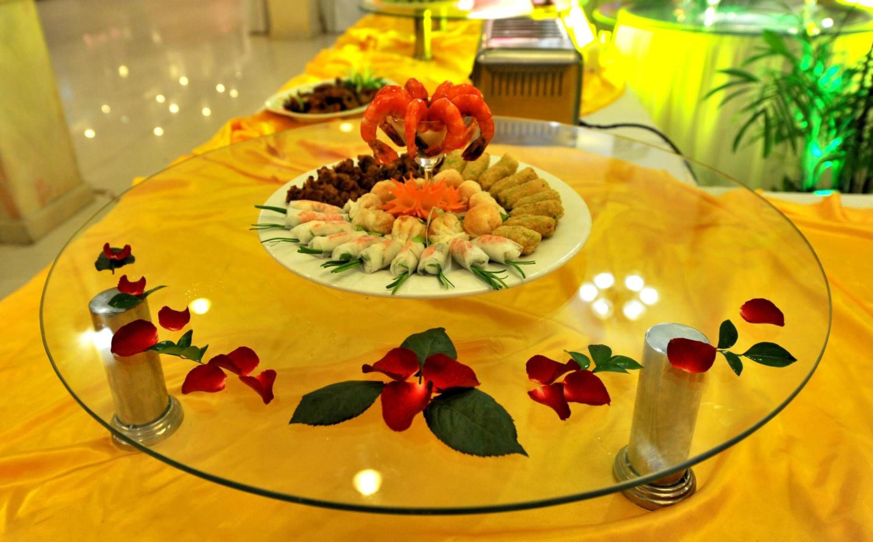A table with a glass top, decorated with food and rose petals.
