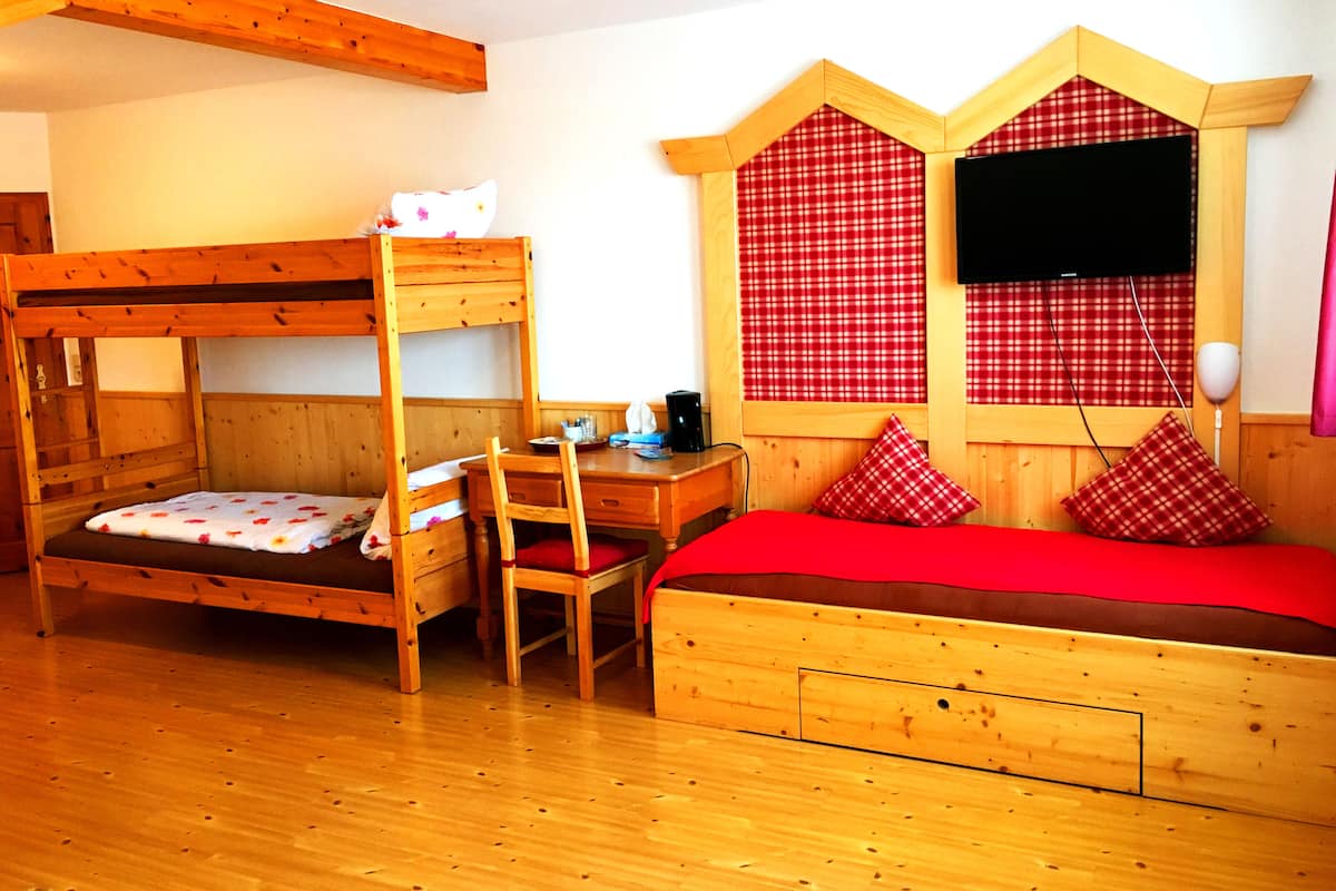 A wooden bunk bed room with a desk and chair, a television, and checkered curtains.