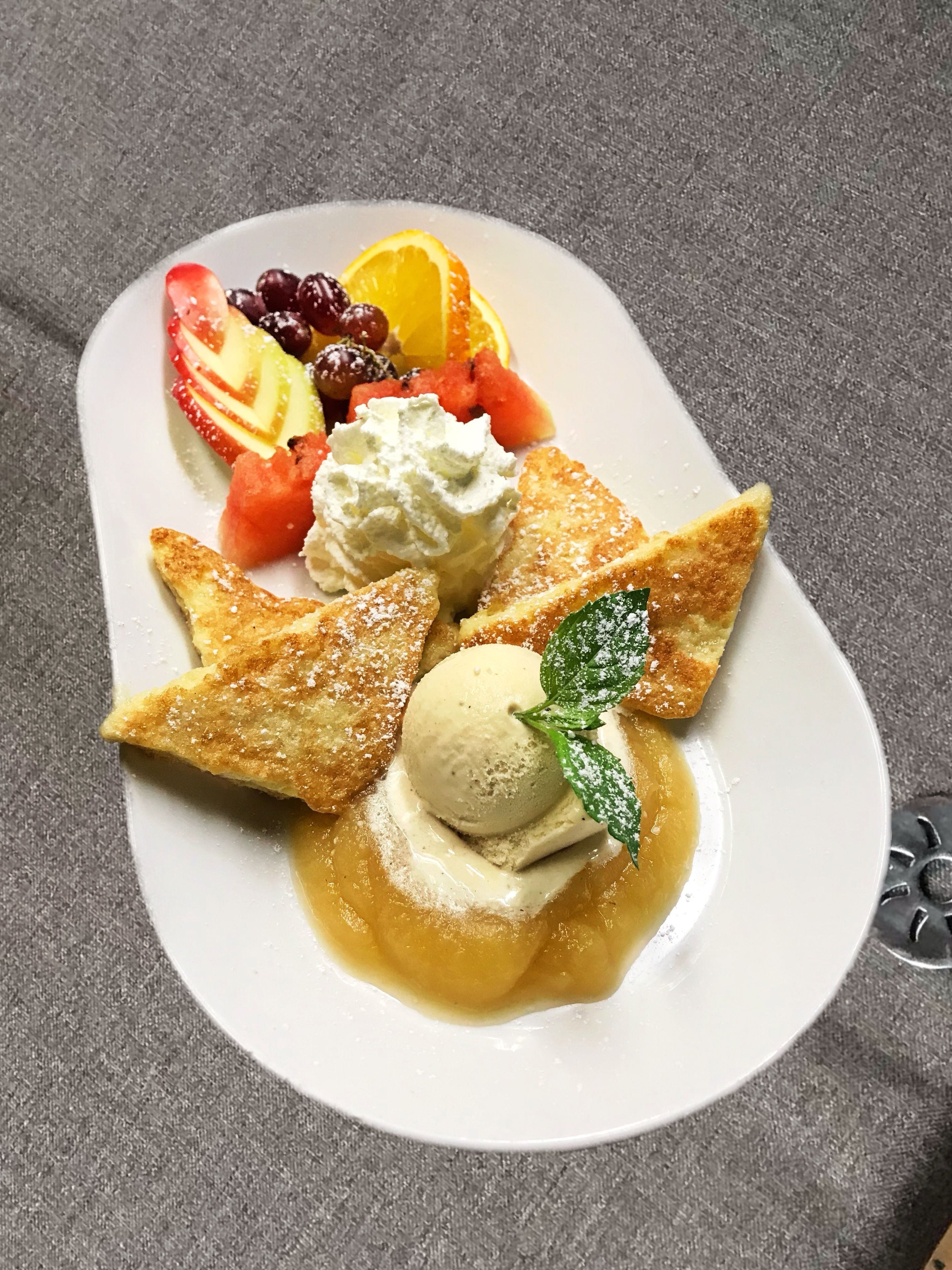 A dessert plate with various fruits, ice cream, and a mint leaf garnish.