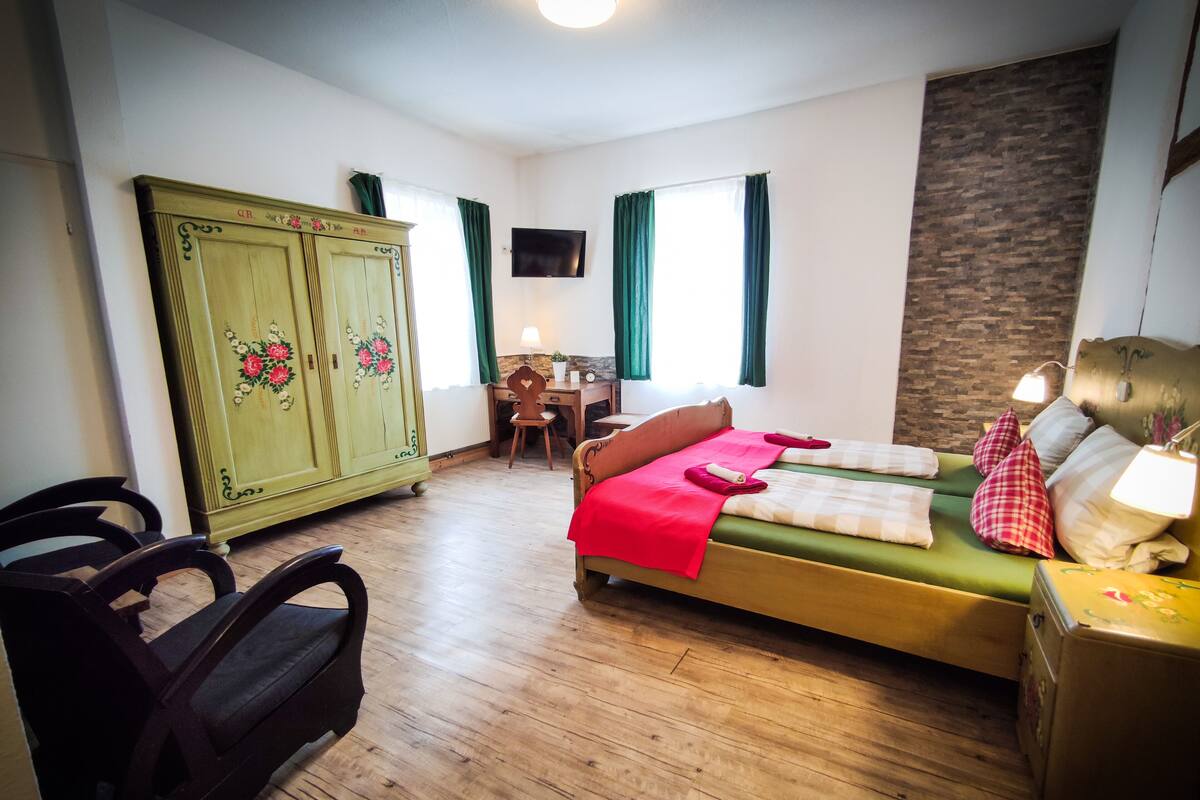 A bedroom with a bed, a desk, a chair, a wardrobe, and a television.