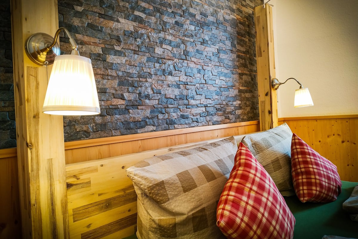 A cozy room with a wooden bench, plaid pillows, and a stone wall.