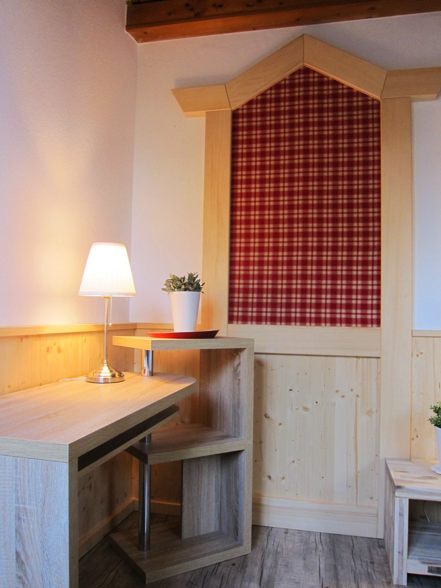 A cozy corner with a wooden table, a lamp, a small potted plant, and a red plaid curtain.