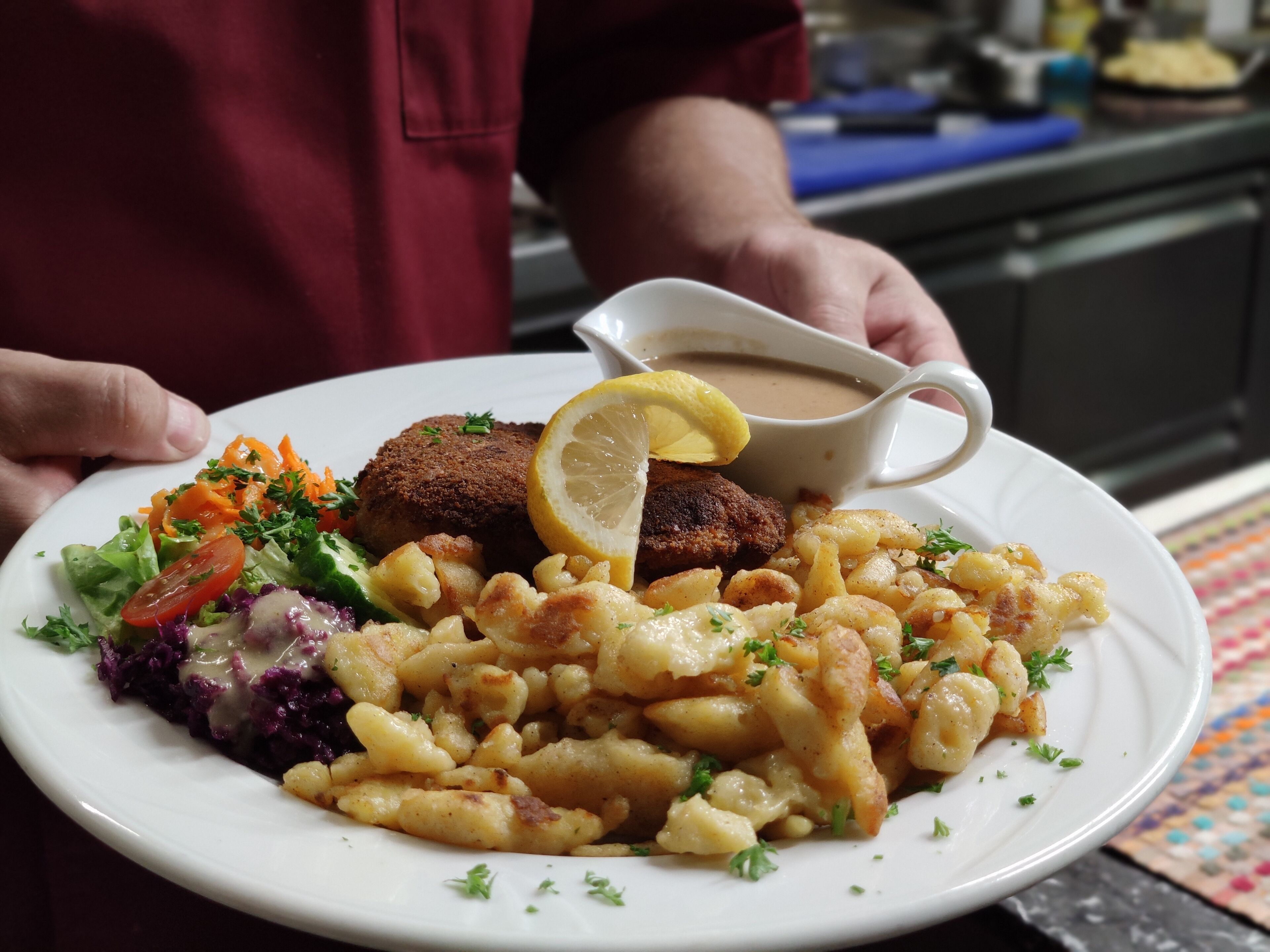A plate of food including meatballs, potatoes, and salad, with a person holding a gravy boat.