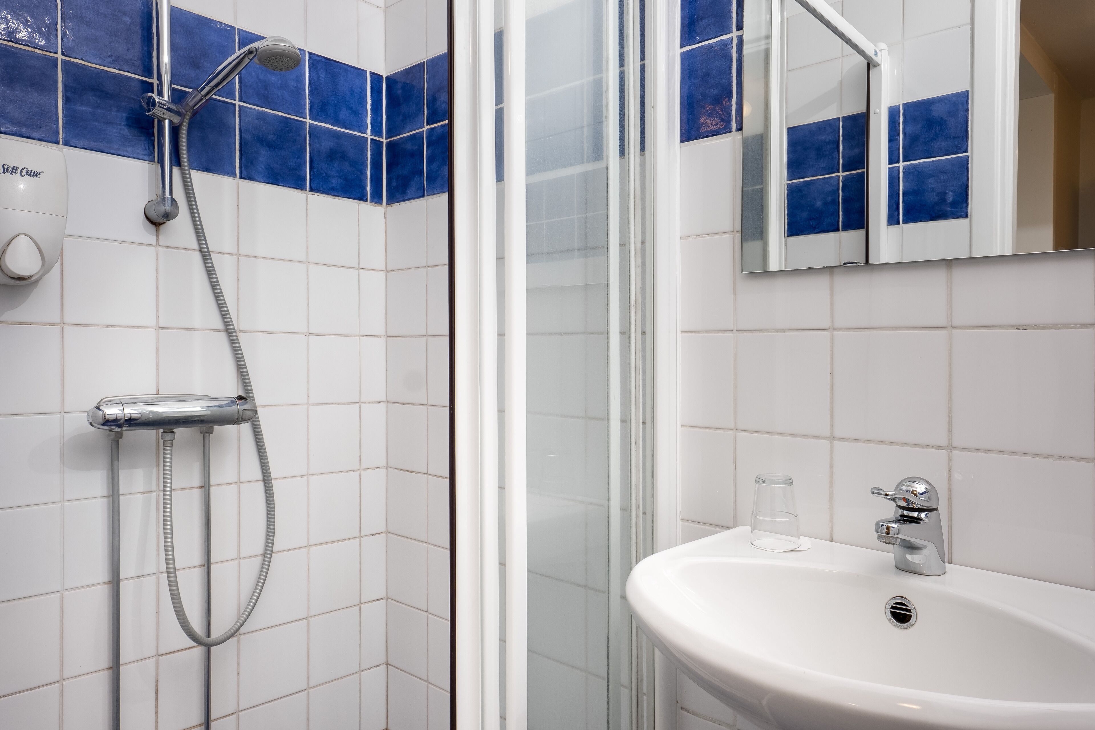 A bathroom with a white sink, a glass, and a shower with a hose.