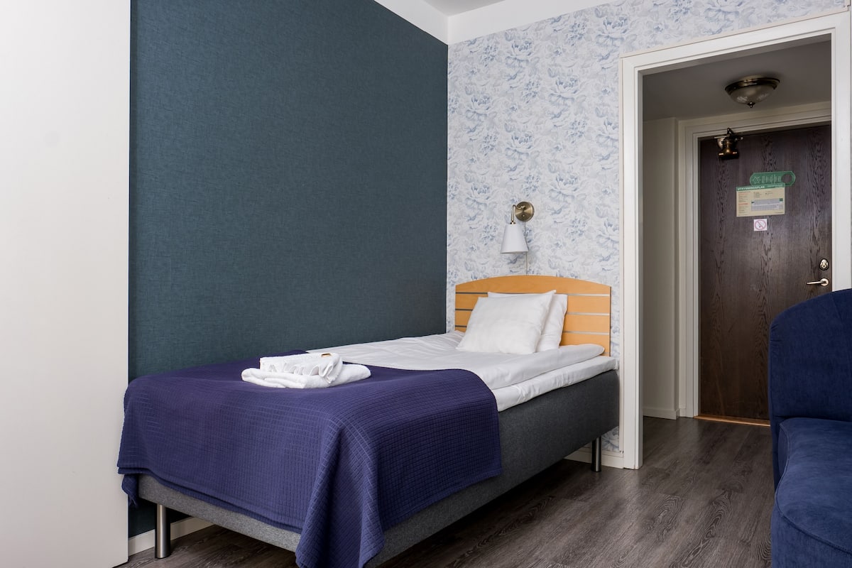 A single bed with a wooden headboard, a white pillow, and a blue blanket.